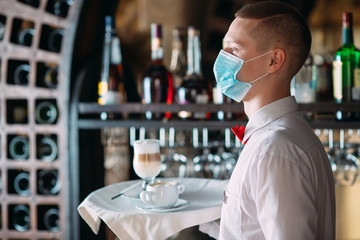 A European-looking waiter in a medical mask serves Latte coffee.