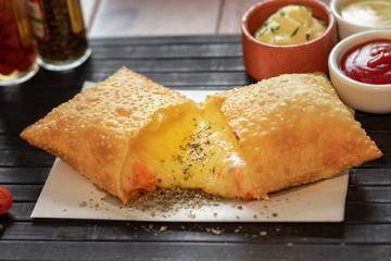 Pastel de quatro queijo com cheddar e mussarela e catupiri e gorgonzola e parmesão em uma mesa com uma esteira preta e guardanapo com fundo de molho 