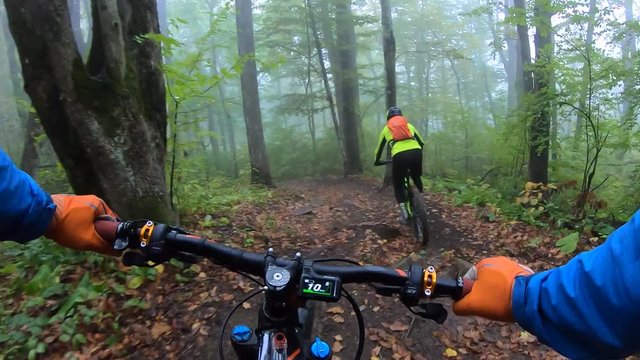 Chest view biker riding on e-bike in a foggy forest between trees. Cyclist rides mountain electro bicycle by autumn foliage in the jungle green summer forests. Extreme enduro ride in the mountains