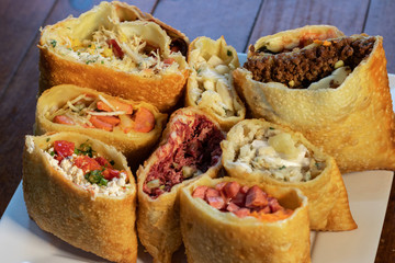 Porção com pastel da culinária  brasileiro com variados sabores em prato branco com fundo de mesa de madeira 