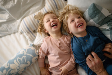 Two small laughing children with unrecognizable father at home, having fun.