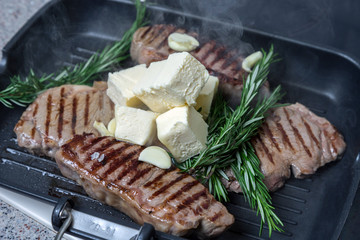 Fried steak in a fluted pan. Meat and rosemary. The oil melts in the pan.