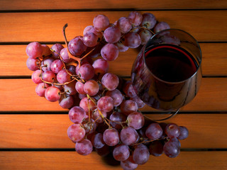 Claster of red grapes and glass of red wine on a wooden table surface. Concept wine making.