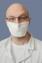 Portrait of a young doctor with glasses and mask, light blue background. Looking at the viewer, Eyes open with quoriosity.