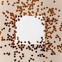 Greeting card with sequins for the inscription, a blank white sheet of paper, gold sparkles in the shape of a heart, top view, copy space, flat lay