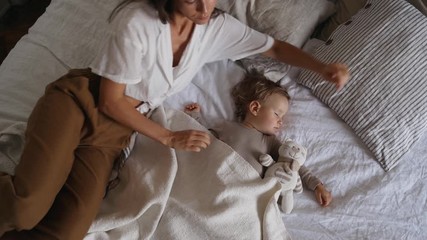 Happy mom is lying with her  sleeping baby girl in bed - Powered by Adobe