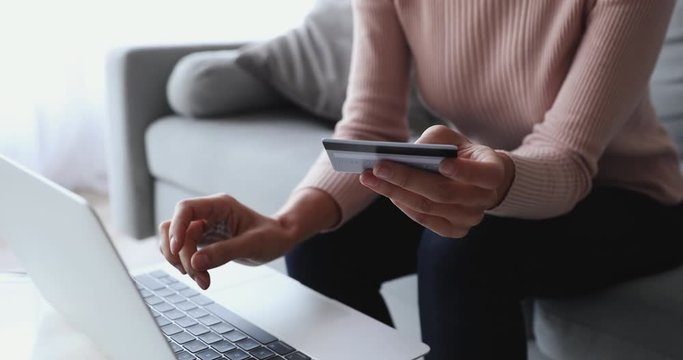 Woman customer using computer e-banking service making secure online payment holding credit card in hand. Female buyer paying on website via e commerce service sitting on sofa at home. Close up view