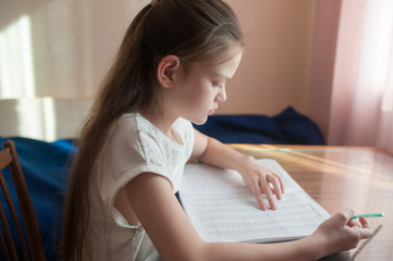 A school-age girl is studying at home at the table. Solves examples in a notebook. Stay at home. Coronovirus.