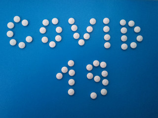 Word covid 19 made of white pills on a blue background