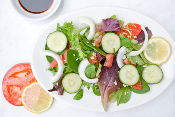 Salad with veggies and balsamic vinegar on a white plate and white table. 