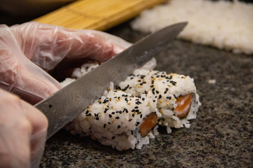 Mãos cortando sushi em close