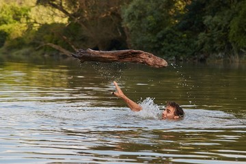Man swimming in a river throwing a driftwood log