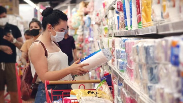 Young woman in a mask from a coronavirus epidemic makes purchases in a supermarket, chooses toilet paper, people in a panic from the global epidemic are buying up everything.