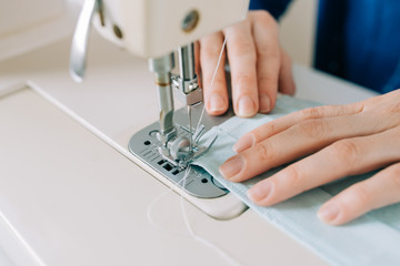 Naklejka premium Woman hands using the sewing machine to sew the face home made diy medical mask during the coronavirus pandemia.