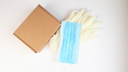 Brown cardboard box,latex white medical gloves and blue medical mask on a white background,top view.Safe delivery of online orders during the coronavirus epidemic,COVID-19,2019-nCoV.