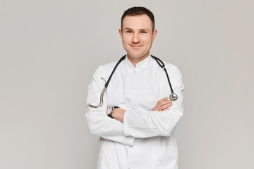 Portrait of handsome doctor posing in medical uniform with stethoscope on grey background. Concept of healthcare and professional medicine