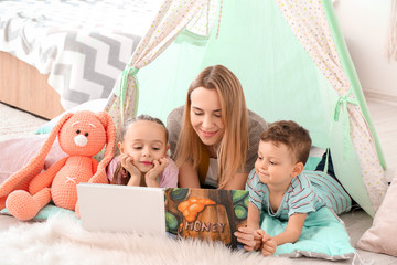 Nanny and cute little children reading book at home