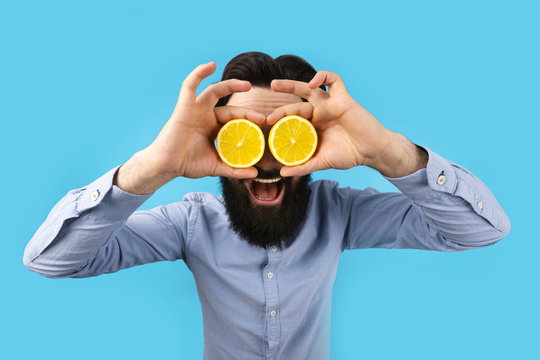 smiling hipster man holding lemon slices in front of eyes, over blue background, fruit and healthy organic food, citrus vitamin - Powered by Adobe