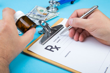 Male doctor or pharmacist holding jar or bottle of pills in hand and writing prescription on a special form. medical costs and healthcare payment concept.