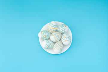 Decorated Easter eggs lie on the white plate on blue background. Happy Easter holiday concept. Greeting, invitation card. Flat lay style with copy space.