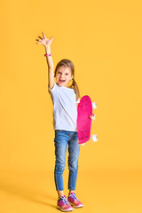 Stylish funny girl wearing white t-shirt, blue jeans and sneakers, holding skateboard over yellow background.