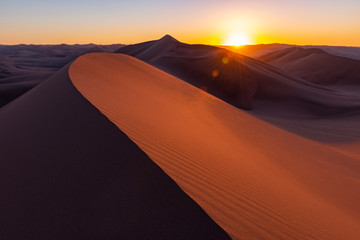 Fototapeta na wymiar Shadow and Light at sunset in the giant sand dunes of the desert between Ica and Huacachina, Peru. Foreground sharp, background unsharp, lens flare.