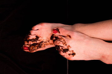 Girl's dirty bare feet stained with mud with painted red nails. On a black background