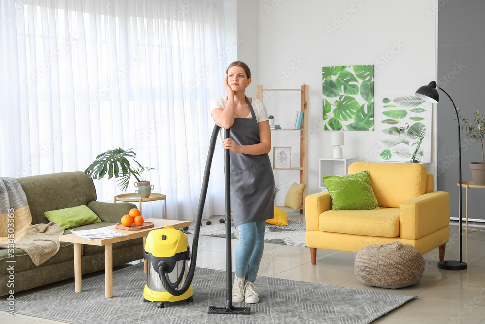 Wall mural young woman hoovering floor at home