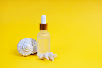 Fototapeta na wymiar Face care in a glass dropper bottle with sea shell and coral on a yellow background. Skin care concept.