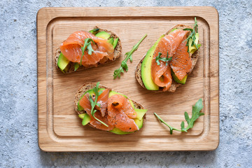 Sandwich with avocado and salmon on a wooden board, top view.