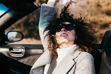 Curly beautiful woman in a convertible car on a sunny day in sunglasses relaxes and feels freedom...