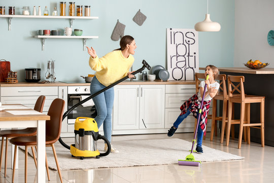 Young woman with her little daughter having fun while cleaning kitchen
