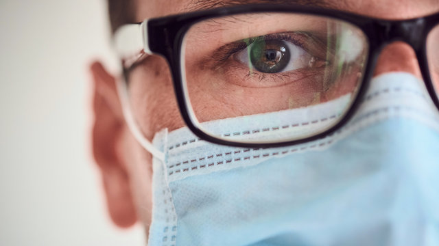Close-up of young man face in medical mask and glasses looking at the camer