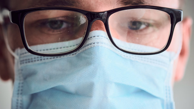 Close-up Portrait Of Young Sad And Tired Doctor In Misted Glasses And Medical Mask Looking Into Camera