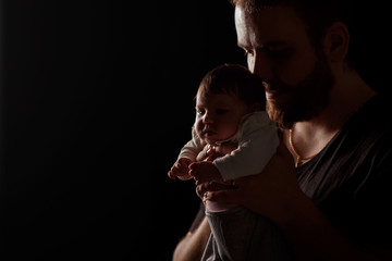 a bearded father in a black t-shirt holds a newborn baby. Dad kisses and hugs daughter or son on a black background