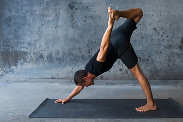 Man practicing yoga in front of a dark background, variation of three legged dog. 