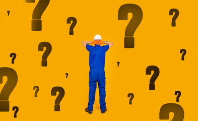 Rear view of a male builder in a helmet with his hands on his head, standing in front of a wall with many questions, was left without work in the conditions of the economic crisis.