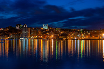 St. John's waterfront harbour at night during the blue hour. The lights on the water are bright yellow and orange which are reflecting from the skyline in the stillness of the smooth water.  