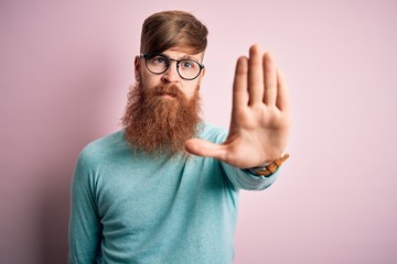 Handsome Irish redhead man with beard wearing glasses over pink isolated background doing stop sing...