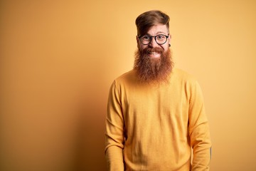 Obraz premium Handsome Irish redhead man with beard wearing glasses over yellow isolated background with a happy and cool smile on face. Lucky person.