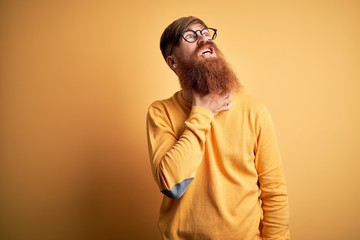 Fototapeta premium Handsome Irish redhead man with beard wearing glasses over yellow isolated background Touching painful neck, sore throat for flu, clod and infection