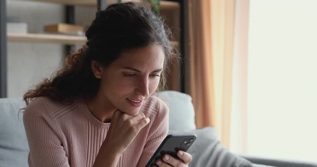 Smiling millennial woman watching funny video stories on smart phone at home. Happy female customer doing mobile shopping, reading news, using apps, surfing internet looking at cell sitting on couch. - Powered by Adobe
