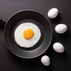 Fried egg in black frying pan with raw white eggs on a black table