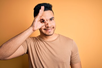 Fototapeta na wymiar Young handsome man wearing casual t-shirt standing over isolated yellow background doing ok gesture with hand smiling, eye looking through fingers with happy face.