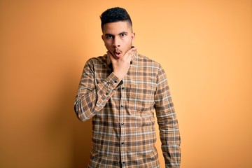 Young handsome man wearing casual shirt standing over isolated yellow background Looking fascinated with disbelief, surprise and amazed expression with hands on chin