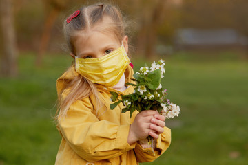 Little child girl in a protective mask holds a spring bouquet of flowers in the garden in the fresh...