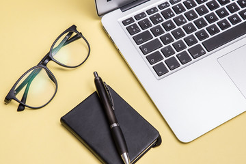Book, laptop, pen, glasses, yellow background