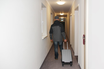 adult man goes down the hotel corridor to his room with a suitcase and keys in his hand, the concept of a long-awaited vacation, business trip