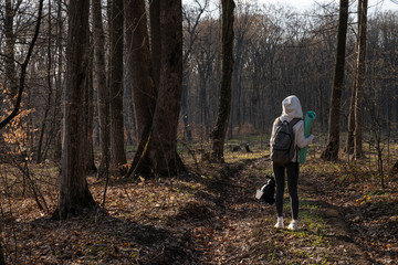 Obraz premium Young girl in sportswear with with grey backpack stands among the forest and dirt road and holding blue yoga mat