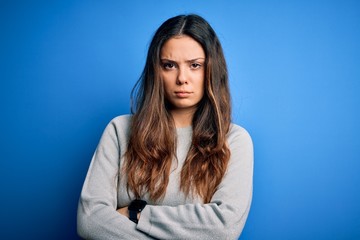 Young beautiful brunette woman wearing casual sweater standing over blue background skeptic and nervous, disapproving expression on face with crossed arms. Negative person.